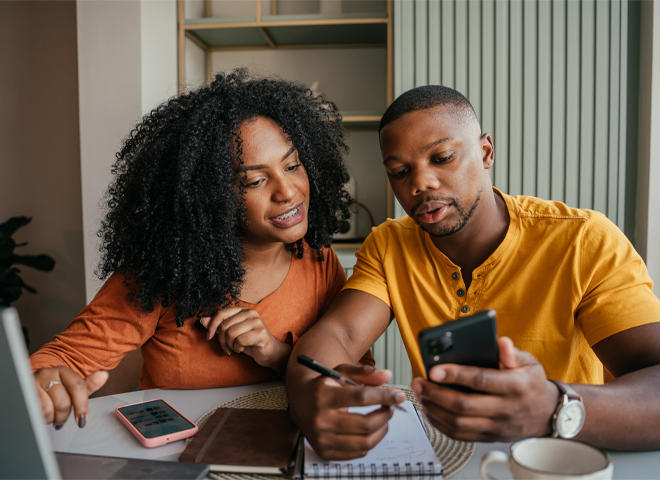two people looking a phone while sitting at a table.